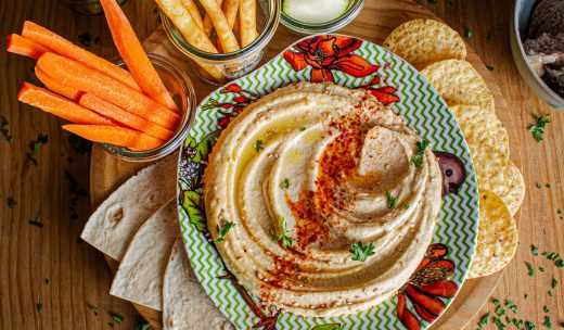 Hummus vegano casero servido con pan pita, bastones de vegetales ideal como entrada saludable.